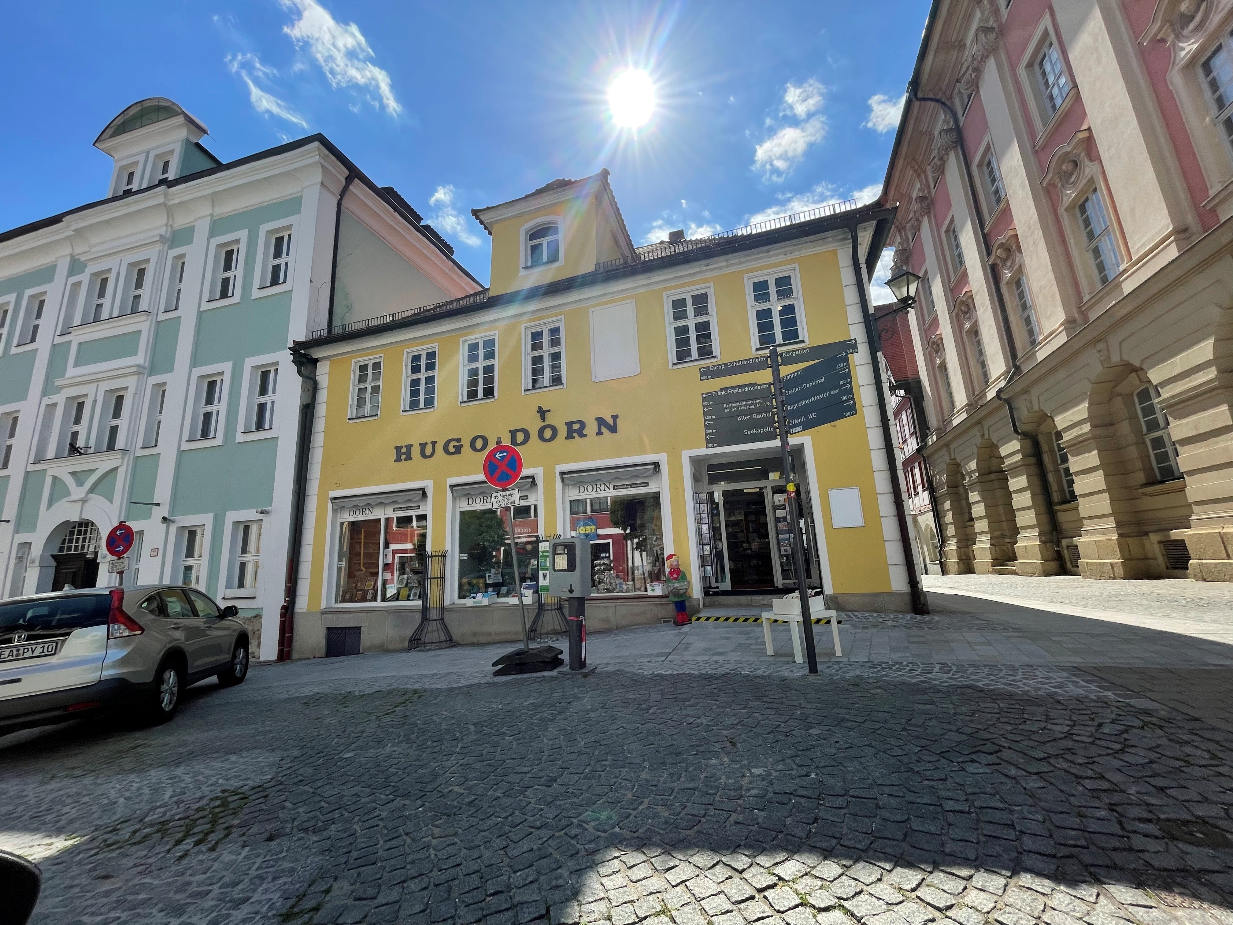 Buchhandlung Dorn Außenansicht. Gepflasterte Straße, gelbe Fassade mit Schaufenstern.